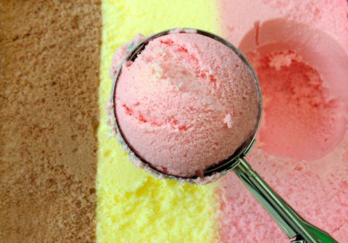 Icecream scoop with chocolate, vanilla and strawberry flavors in the background