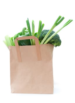 Brown paper bag with healthy green vegetables over a white background 