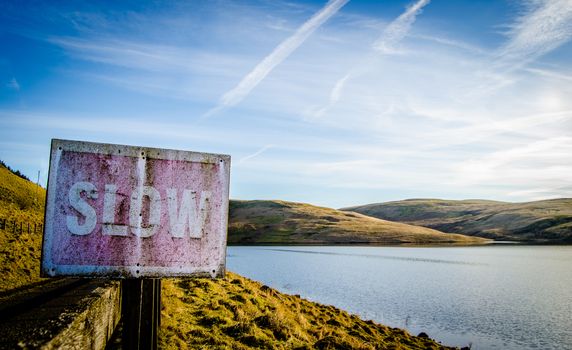 Conceptual Image Of Rustic Slow Sign Beside Tranquil Scenic Lake