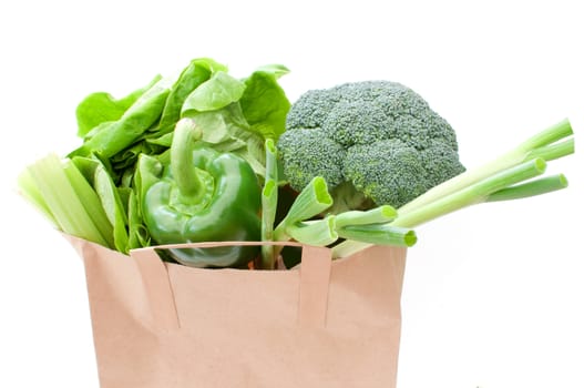 Brown paper bag with healthy green vegetables over a white background 