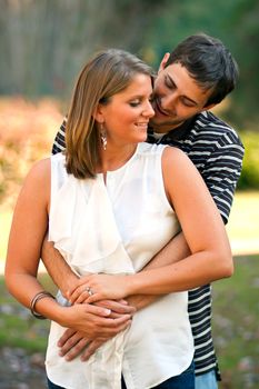 A young couple in love playfully embrace in a pretty wooded area. 