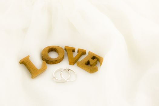 closeup love wording and rings on dress, white soft textiles, wedding and anniversary  concept and idea