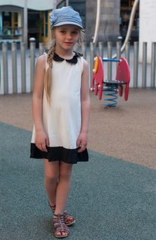 Young girl in white dress and denim cap on the playground