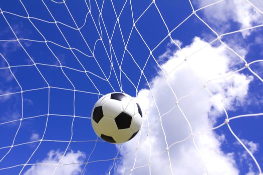 Soccer ball in goal net over blue sky background