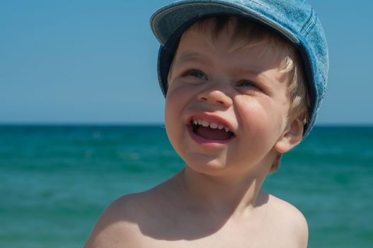 Lovely little boy in denim cap on the beach