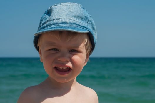 Cute little boy in denim cap on the beach