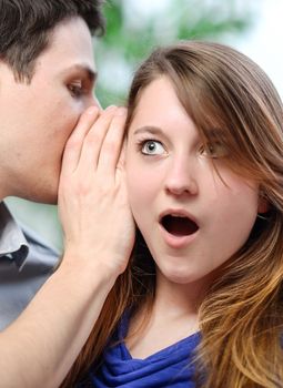 man whispering in the ear of his surprised wife