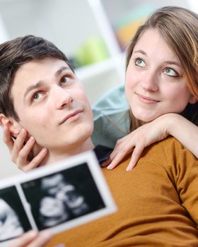 Beautiful couple imagines the future of their unborn child with ultrasound pictures in hands