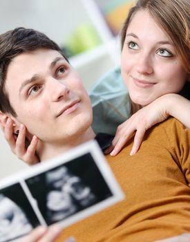 Cute couple imagines the future of their unborn child with ultrasound pictures in hands