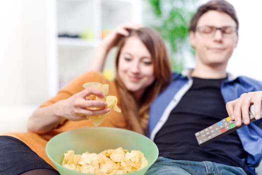 Beautiful young couple watching tv and eating on a sofa