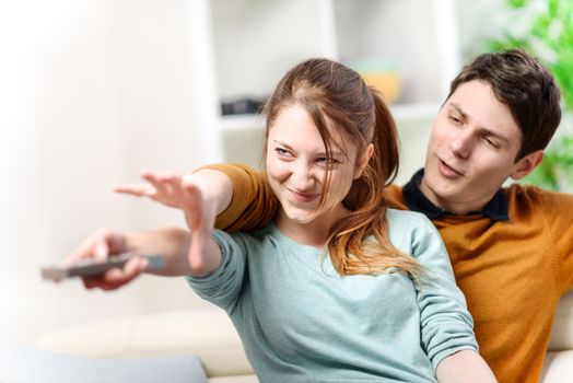 beautiful couple bickering to change tv channel on remote control