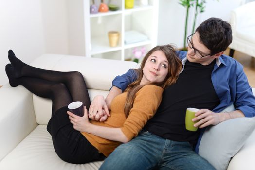 Attractive couple of lovers sitting on a sofa taking a hot drink