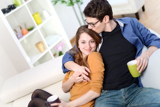 Attractive couple of lovers sitting on a sofa taking a hot drink