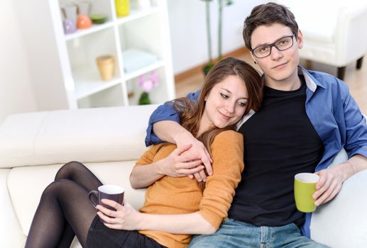 Attractive couple of lovers sitting on a sofa taking a hot drink