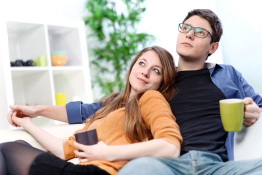 Attractive couple of lovers sitting on a sofa taking a hot drink