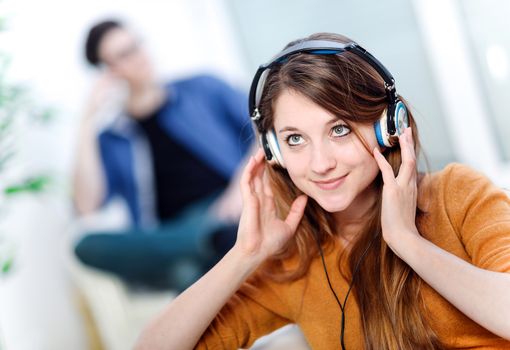 Beautiful blond listening to some music while her boyfriend is bored