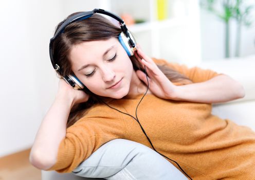 Beautiful relaxed young woman listening of the music by being lengthened on its sofa