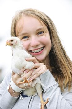 Smiling teenage girl with braces holding young chicken