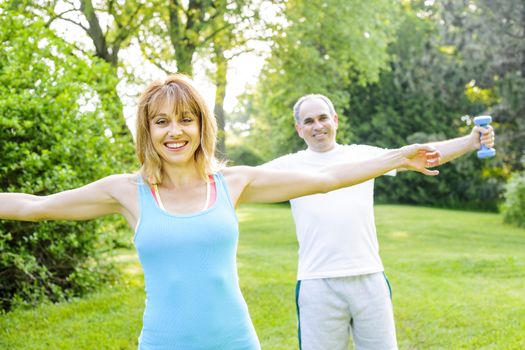Female fitness instructor exercising with middle aged man outdoors in summer park