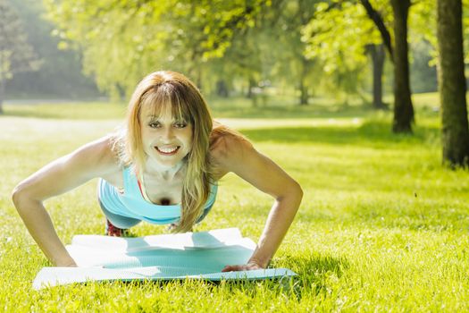 Female fitness instructor exercising doing pushups in green summer park
