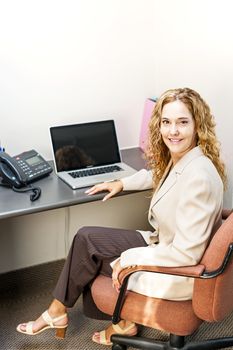 Happy businesswoman sitting at workstation in office with computer