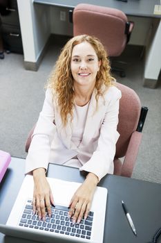Smiling businesswoman sitting at workstation in office with computer