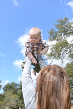 mom playing with baby by flying him through the air outdoors