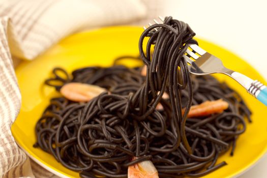 Black spaghetti with prawns on yellow plate