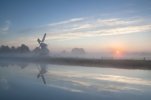 misty sunrise over river and windmill, Holland