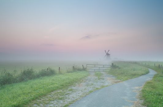 road to Dutch windmill in morning fog, Groningen, Netherlands
