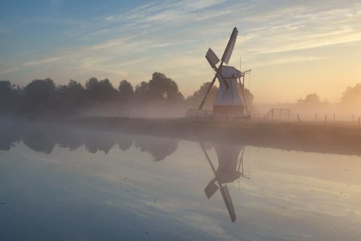 windmill in morning sunshine reflected in river, Holland