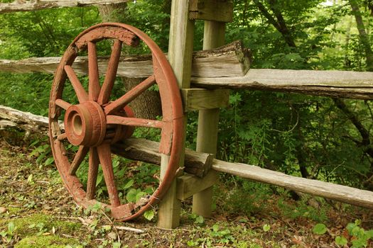 A rustic old wooden wheel against a fence
