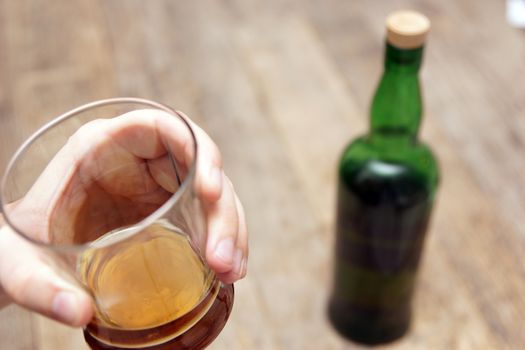 A man holding a glass of scotch next to a bottle