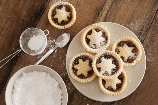 Traditional Christmas fruit mince pies decorated with pastry stars on a kitchen table ready to be sprinkled with powdered icing sugar in a sieve for a delicious seasonal teatime snack, overhead view