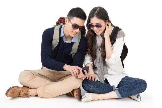 Happy traveling Asian couple sitting on ground and using cellphone, full length portrait on white background.