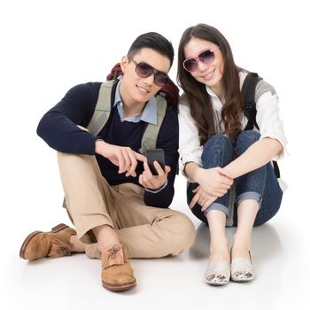 Happy traveling Asian couple sitting on ground and using cellphone, full length portrait on white background.
