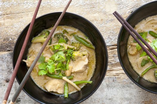 Bowls of tasty Thai green curry served with chopsticks made from nutritional bean sprouts, broccoli, chicken, coconut milk, coriander,and green beans, view from above