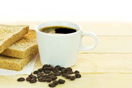 Delicious breakfast with toast, white cup coffee with coffee beans on wood table