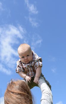 mother holding flying baby boy up against blue sky with a smile