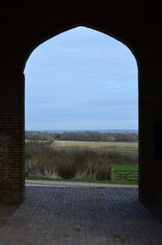 Brick arched entrance leading to open Kent countryside.