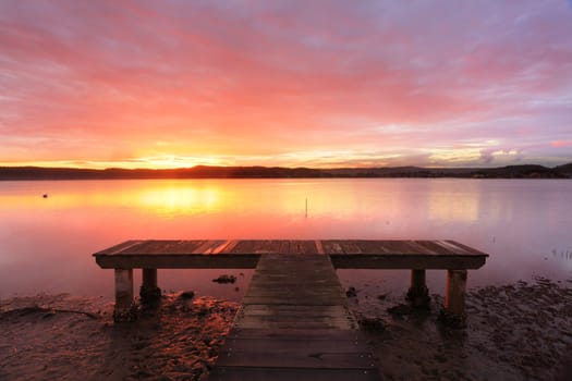 Pretty romantic sunset with red and pink sky at Green Point jetty at low tide with lone pelican on the tranquil waters.   Australia