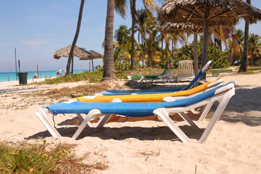 Yellow and blue sun loungers in the sands of a Caribbean paradise beach in Varadero, Cuba with ocean and palm trees  in the background
