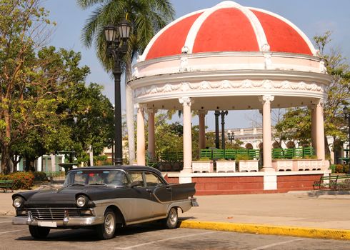 Plaza Jose Marti, a city square in Cienfuegos, Cuba showing bandstand and a classic car under sunny skies