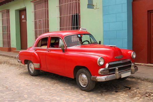 Bright red old fashioned, retro, taxi cab with colorful building backdrop in Trinidad, Cuba