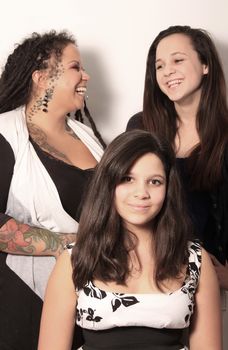 Mother with tattoos, piercings and dreadlocks has some fun with her two daughters on white background containing some shadow, focus on girl in front