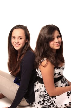 Pretty young teen girls that could be sisters of friends smiling, both with long brown hair on a white background