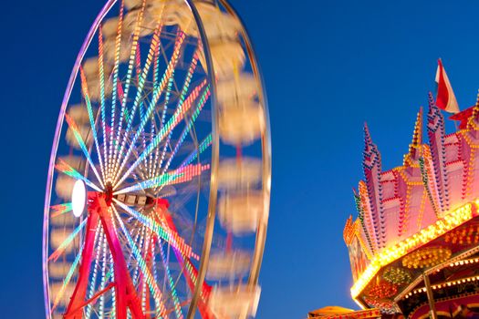 The circular motion of a carnival ferris wheel blurs against a cobalt blue twilight sky at a county fair. 