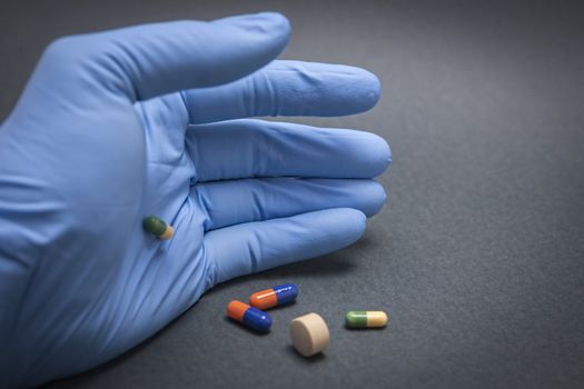 Hand with blue latex glove turning various pills