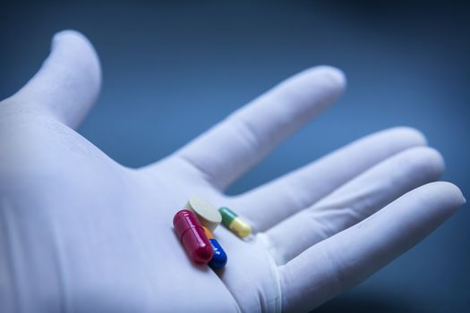 Hand with blue white glove turning various pills