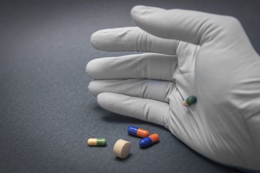 Hand with blue white glove turning various pills